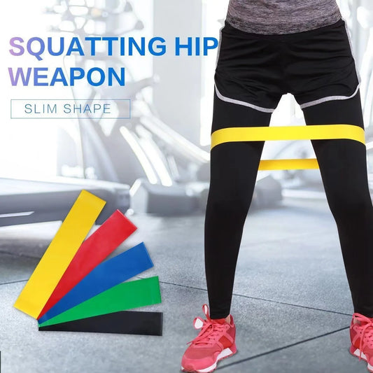 Person wearing black leggings with a yellow resistance band, with fitness equipment in the background.